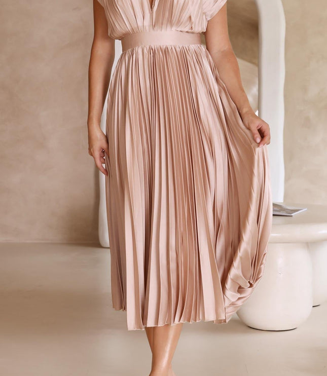 Front view of a women's light pink pleated v-neck midi dress, with a wide waistband and flowing skirt, paired with clear heels.