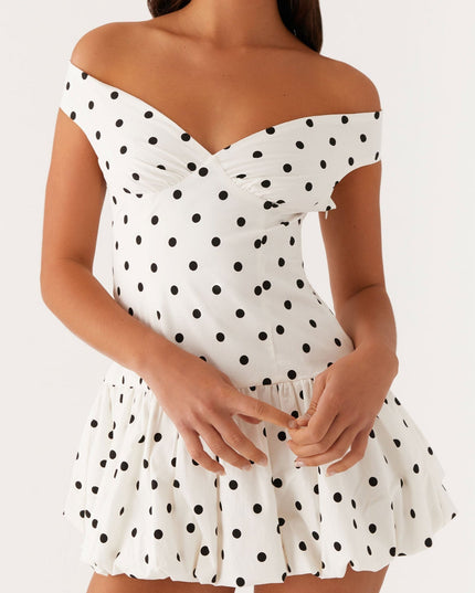 Detail of a white polka dot off-shoulder mini dress, showing the ruched bust and gathered bubble hem.
