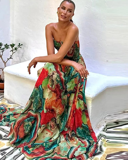 Seated woman in a colorful abstract printed strapless maxi dress, showcasing the flowing skirt and vibrant pattern.