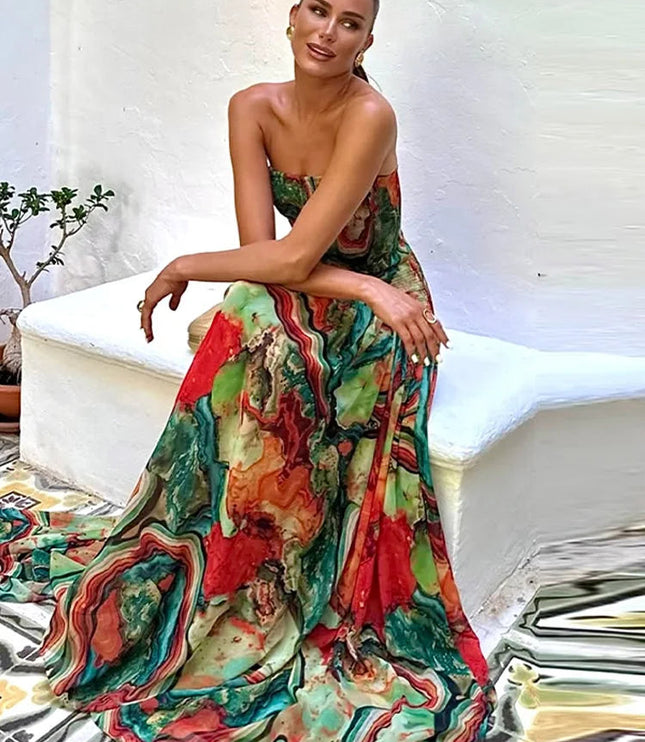 Seated woman in a colorful abstract printed strapless maxi dress, showcasing the flowing skirt and vibrant pattern.