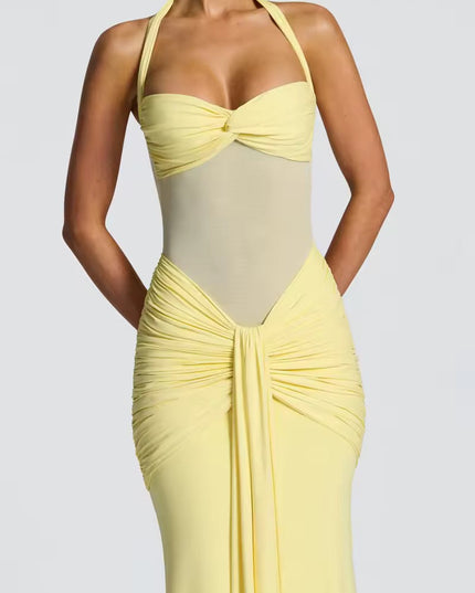 Close-up of a women's light yellow halter neck maxi dress with ruched details and sheer mesh midriff.