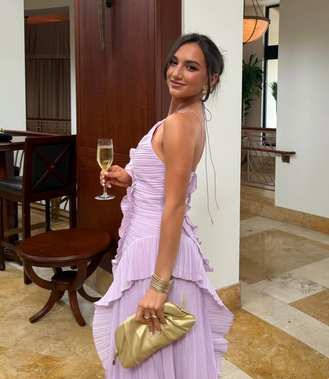 Side profile of the lavender one-shoulder midi dress, showing the pleated skirt and ruffled details, accessorized with a gold clutch.