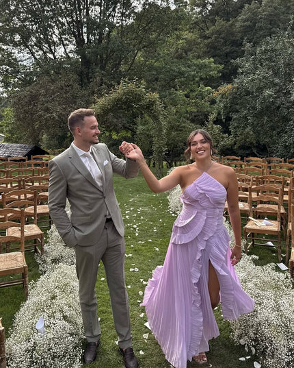 Women's lavender one-shoulder ruffle midi dress with a high slit, worn at an outdoor wedding with a man in a sage green suit.