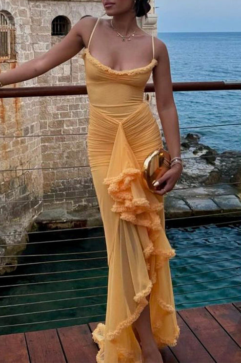 Women's yellow prom ruffled front maxi dress worn outdoors by the water, holding a gold clutch, with layered necklaces.