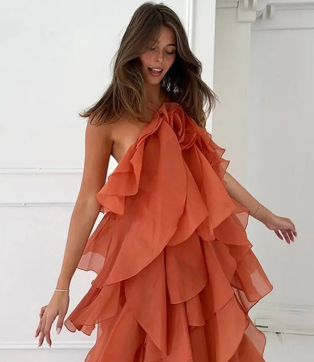 Side view of a woman in a coral strapless ruffle layered maxi dress, showing the flowing tiers and a large floral detail on the bodice.