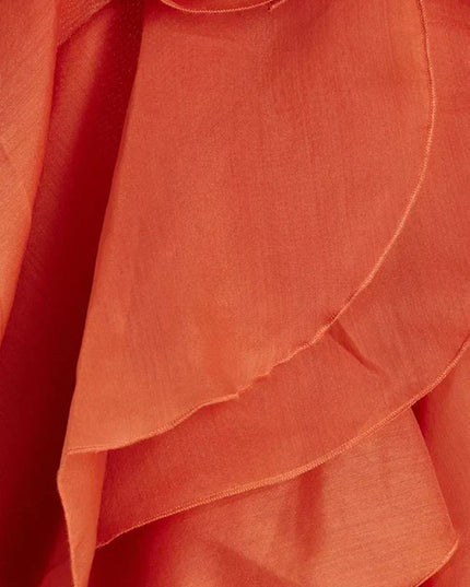 Close-up detail of the coral fabric and layered ruffles of the strapless maxi dress, showing the texture and construction of the flowing tiers.