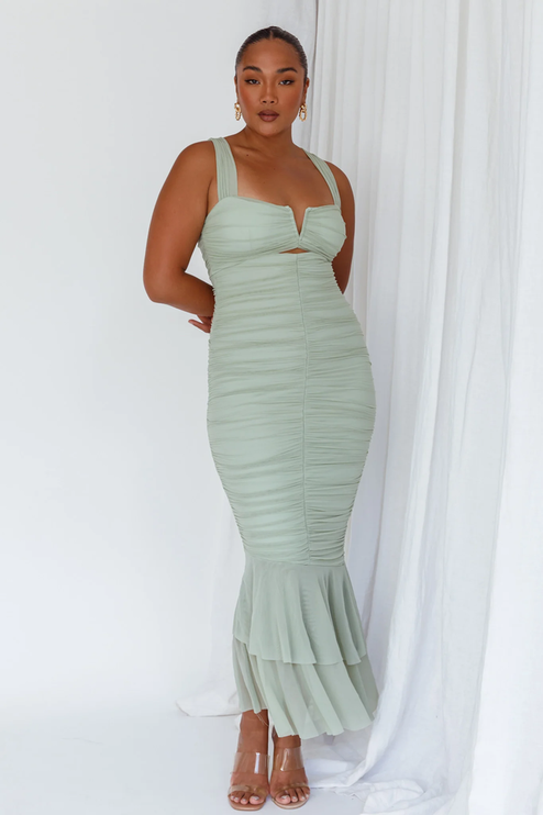Front full-length view of a woman wearing a light green ruched V-neck fishtail maxi dress with clear heels.