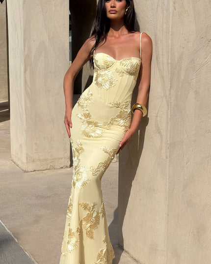 Woman posing in a light yellow floral lace-up maxi dress with gold embroidered flowers, showcasing the elegant fit and flow.