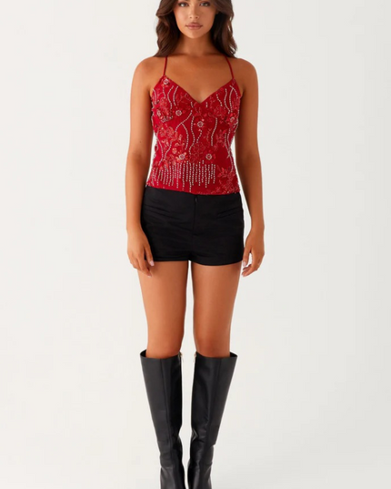 Full body shot of a red sequin V-neck cami top with detailed beadwork, paired with black shorts and knee-high boots.
