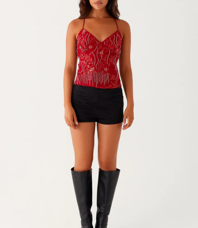 Full body shot of a red sequin V-neck cami top with detailed beadwork, paired with black shorts and knee-high boots.