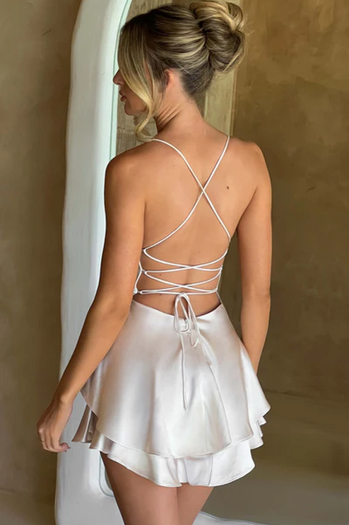 Back view of a women's ivory satin backless mini romper, featuring criss-cross tie straps and ruffled hem.