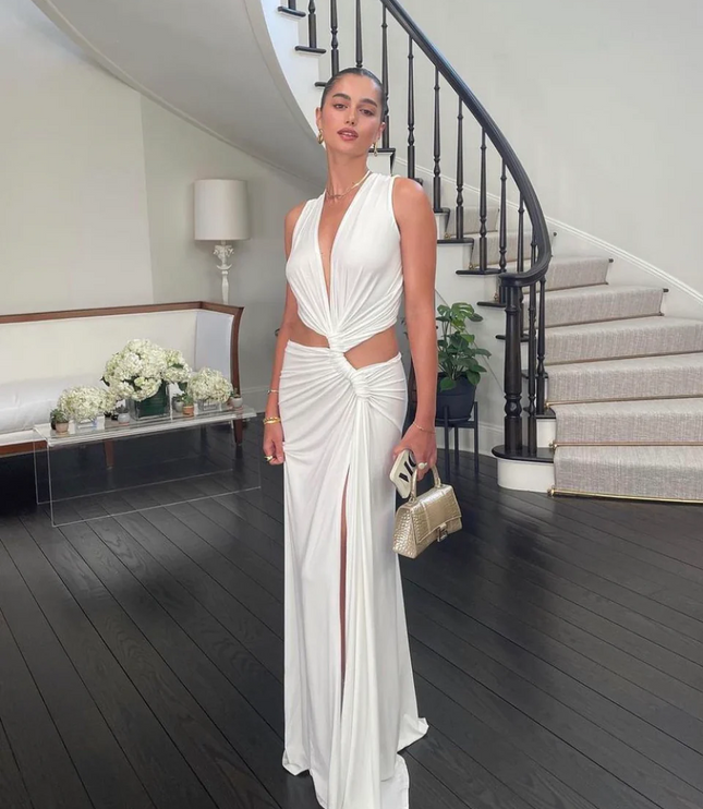 White sleeveless halter V-neck maxi dress with side cut-outs and a high slit, standing indoors.