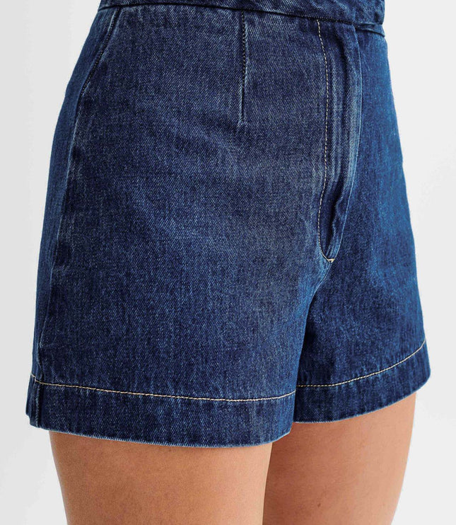 Close-up side view of dark wash denim shorts with a high waist, pleat detail, and contrasting light stitching.