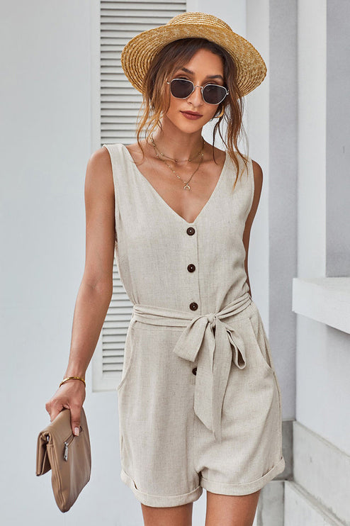 Close-up front view of a women's beige sleeveless V-neck romper with button details and tie waist.