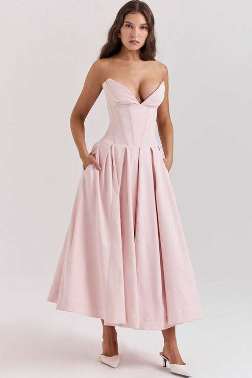 Side view of a pink strapless boned bodice midi dress, showing the pleated skirt and pockets, with white heels.