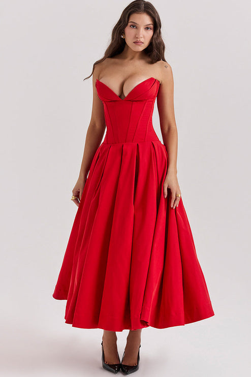 Front view of a woman in a vibrant red strapless boned bodice pleated midi dress and black slingback heels.