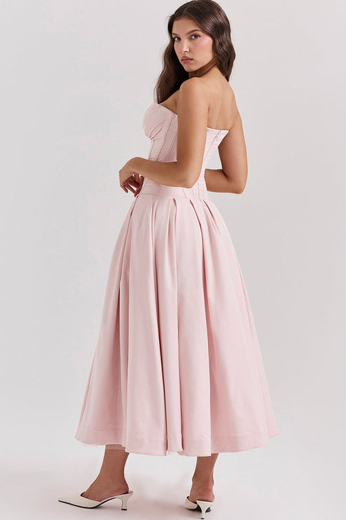 Side profile of a woman in a light pink strapless boned bodice pleated midi dress with white kitten heels.