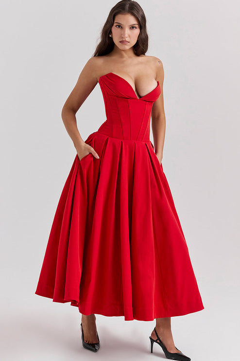 Woman with hands in pockets of a red strapless boned bodice pleated midi dress, highlighting the practical design.