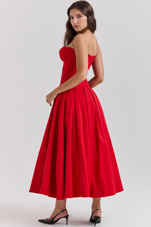 Side view of a woman wearing a red strapless boned bodice pleated midi dress, showing the elegant silhouette.