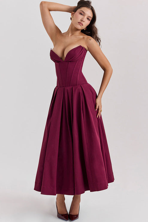 Woman with arm raised, showcasing the movement of a burgundy strapless boned bodice pleated midi dress.