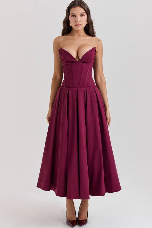 Front view of a woman in a deep burgundy strapless boned bodice pleated midi dress with matching heels.