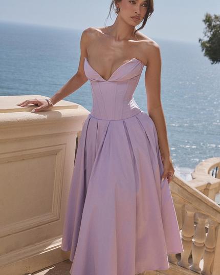 Lavender strapless boned bodice pleated midi dress for women, shown outdoors with ocean background