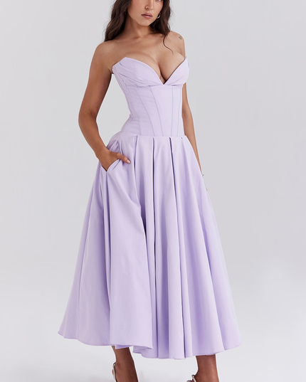 Side profile of a women's lavender strapless boned bodice pleated midi dress with hands in pockets