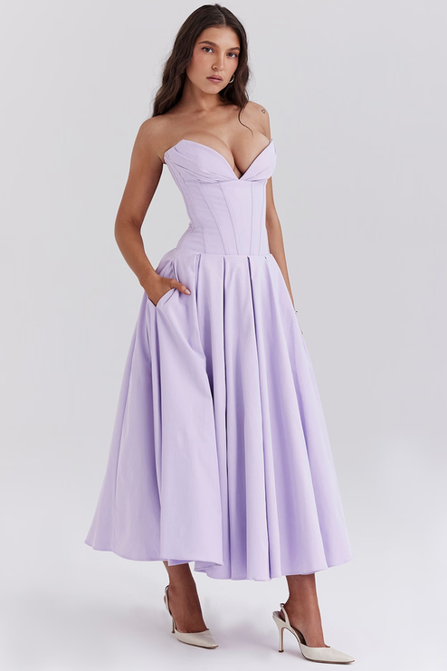 Side profile of a women's lavender strapless boned bodice pleated midi dress with hands in pockets