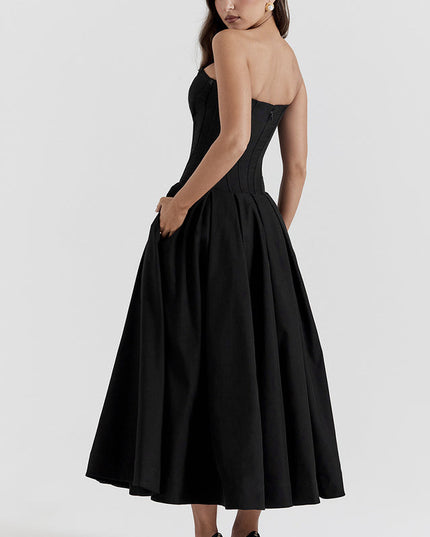 Side view of black strapless boned bodice midi dress with pleated skirt and pockets, black heels.