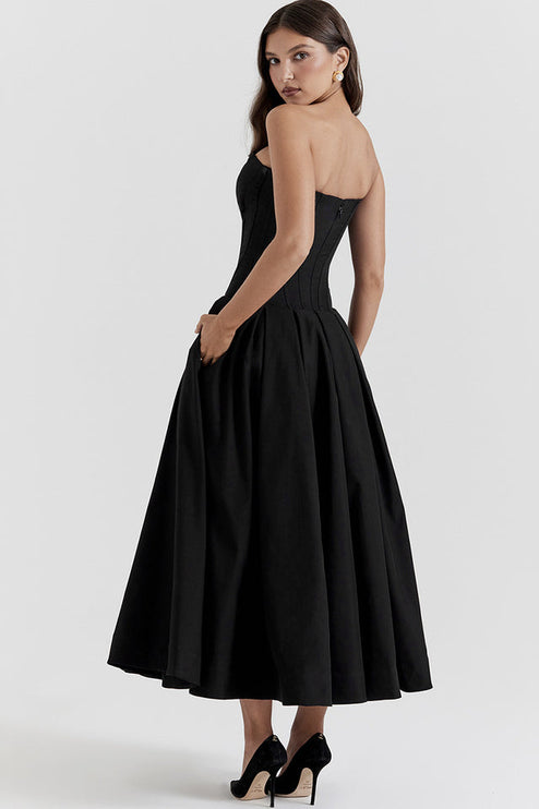 Side view of black strapless boned bodice midi dress with pleated skirt and pockets, black heels.