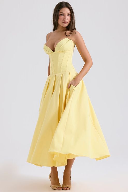 Side view of a women's light yellow strapless boned bodice pleated midi dress, showing pockets