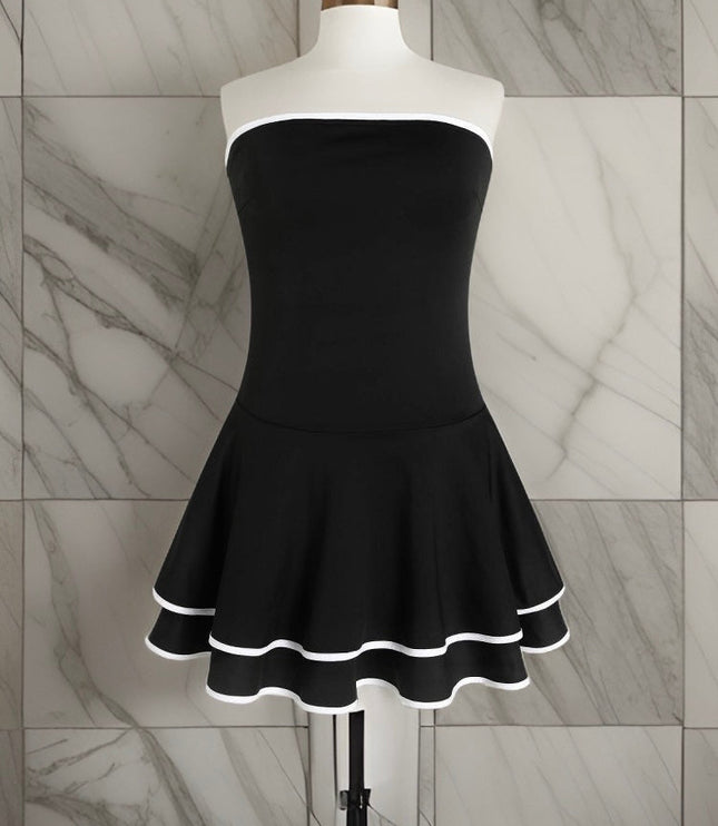 Mannequin wearing a black strapless mini dress with a fitted bodice and a tiered, ruffled skirt with white trim.