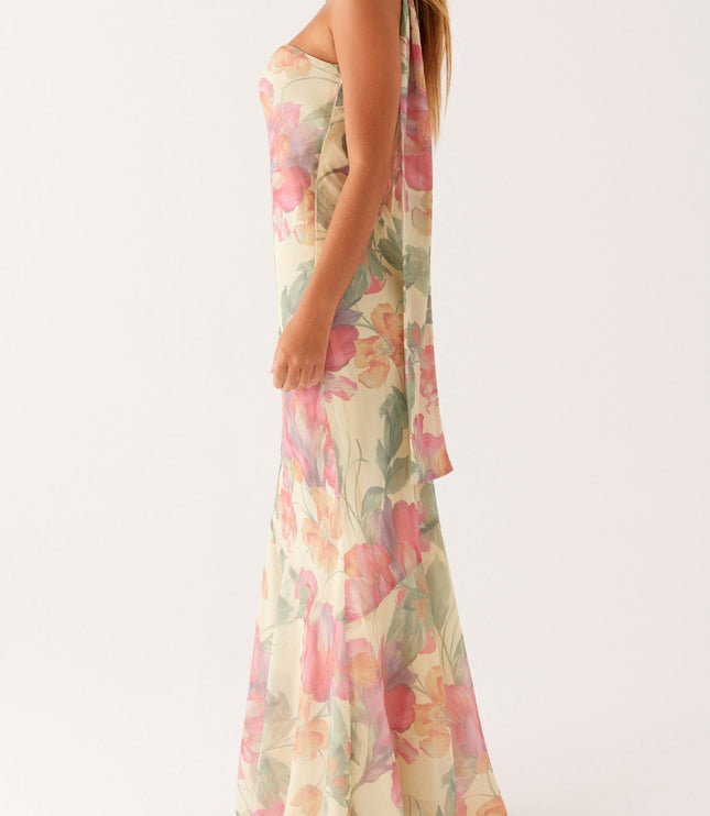 Side profile of a women's floral strapless maxi dress, showcasing the elegant asymmetrical design and attached neck scarf.