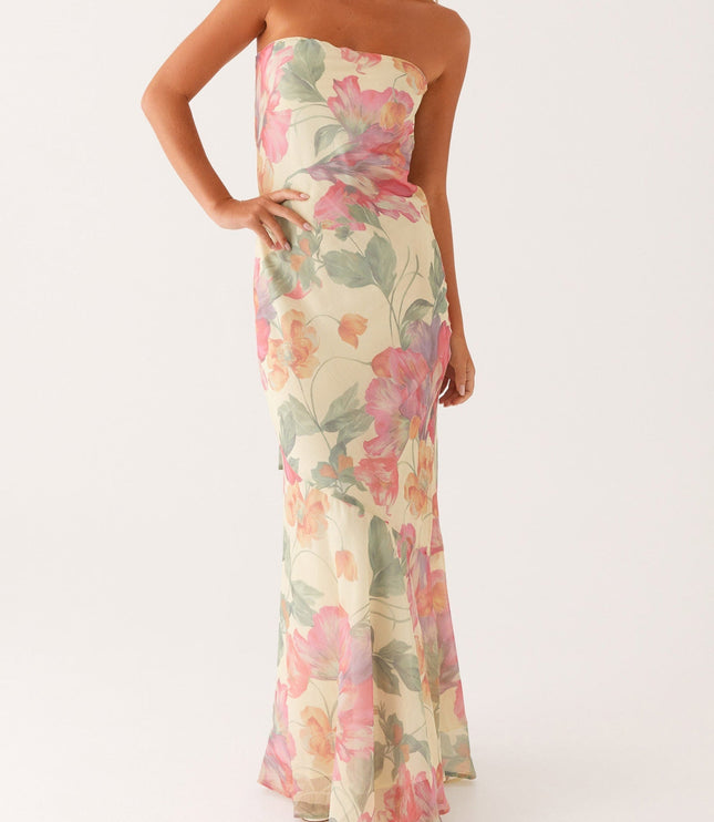 Full length front view of women's strapless floral maxi dress with an asymmetrical hem, styled with white heels.