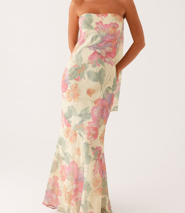 Women's strapless floral maxi dress in light yellow with pink and green flowers, featuring an asymmetrical hem and flowing scarf detail.