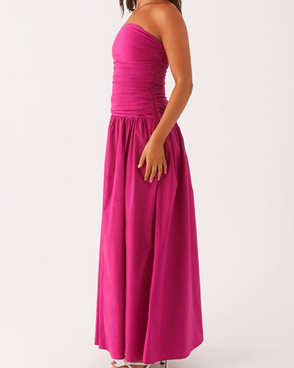 Side profile of a women's bright pink strapless ruched maxi dress, showing the flowing skirt and drop waist.