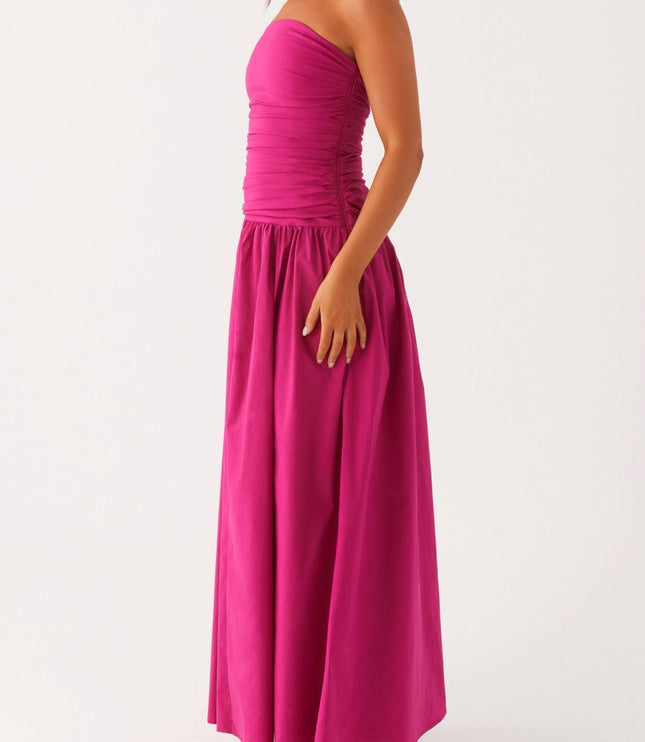 Side profile of a women's bright pink strapless ruched maxi dress, showing the flowing skirt and drop waist.