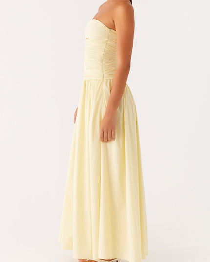 Side profile of a women's pale yellow strapless maxi dress featuring a ruched top and flowing skirt.