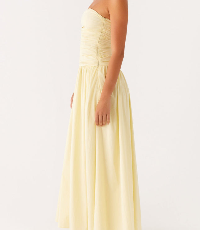 Side profile of a women's pale yellow strapless maxi dress featuring a ruched top and flowing skirt.