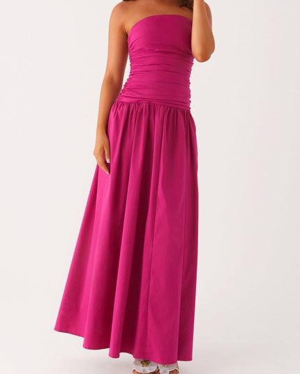 Women's fuchsia strapless ruched maxi dress in a dynamic pose, showing the full skirt and drop waist design.