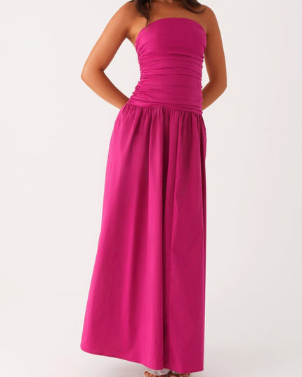 Full front view of a women's fuchsia strapless ruched maxi dress with hands behind back, showcasing the drop waist.