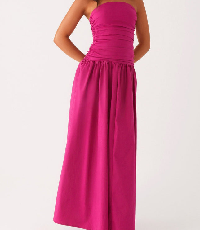 Full front view of a women's fuchsia strapless ruched maxi dress with hands behind back, showcasing the drop waist.