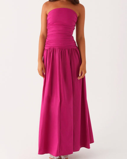 Front view of a women's strapless ruched fuchsia maxi dress with a drop waist, paired with white heels.