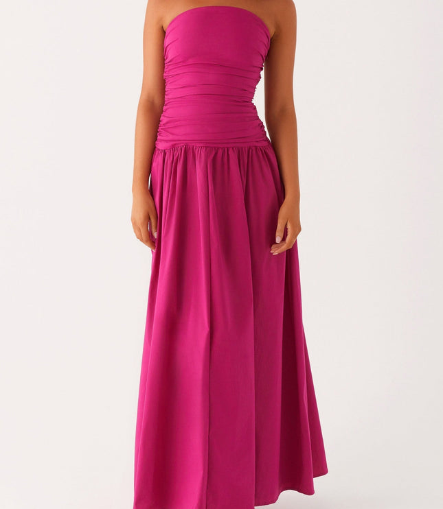 Front view of a women's strapless ruched fuchsia maxi dress with a drop waist, paired with white heels.