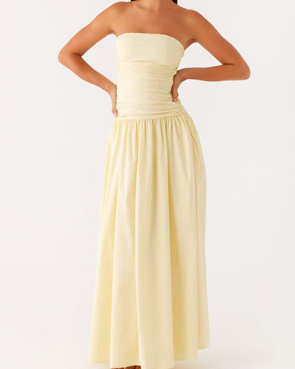 Pale yellow strapless maxi dress with ruched bodice and drop waist, hands on hips pose.
