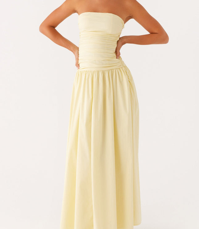 Pale yellow strapless maxi dress with ruched bodice and drop waist, hands on hips pose.