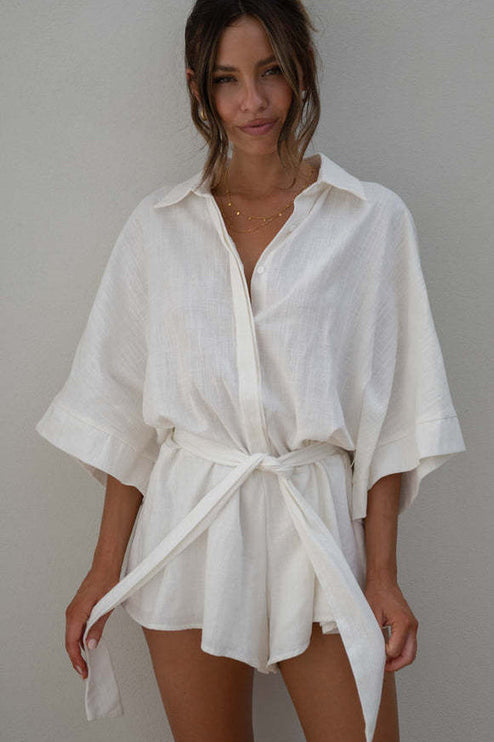 Front view of a white summer collared button-front short romper with a self-tie belt, showcasing the light fabric.