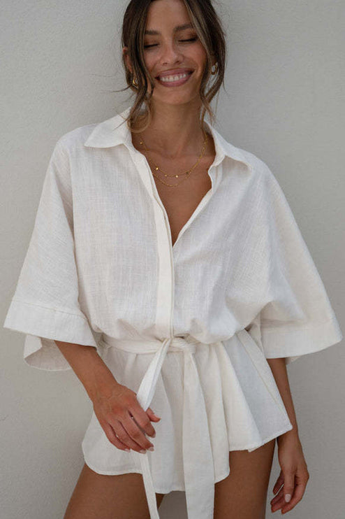 Close-up of a women's summer collared button-front short romper in textured white fabric with a tied waist.