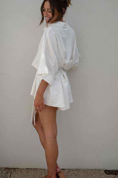 Three-quarter back view of a women's white summer collared short romper, highlighting the loose sleeves and waist tie.