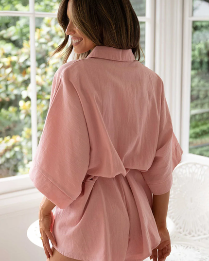 Back view of a woman wearing a pink summer collared button-front short romper, detailing the relaxed fit and tied waist.